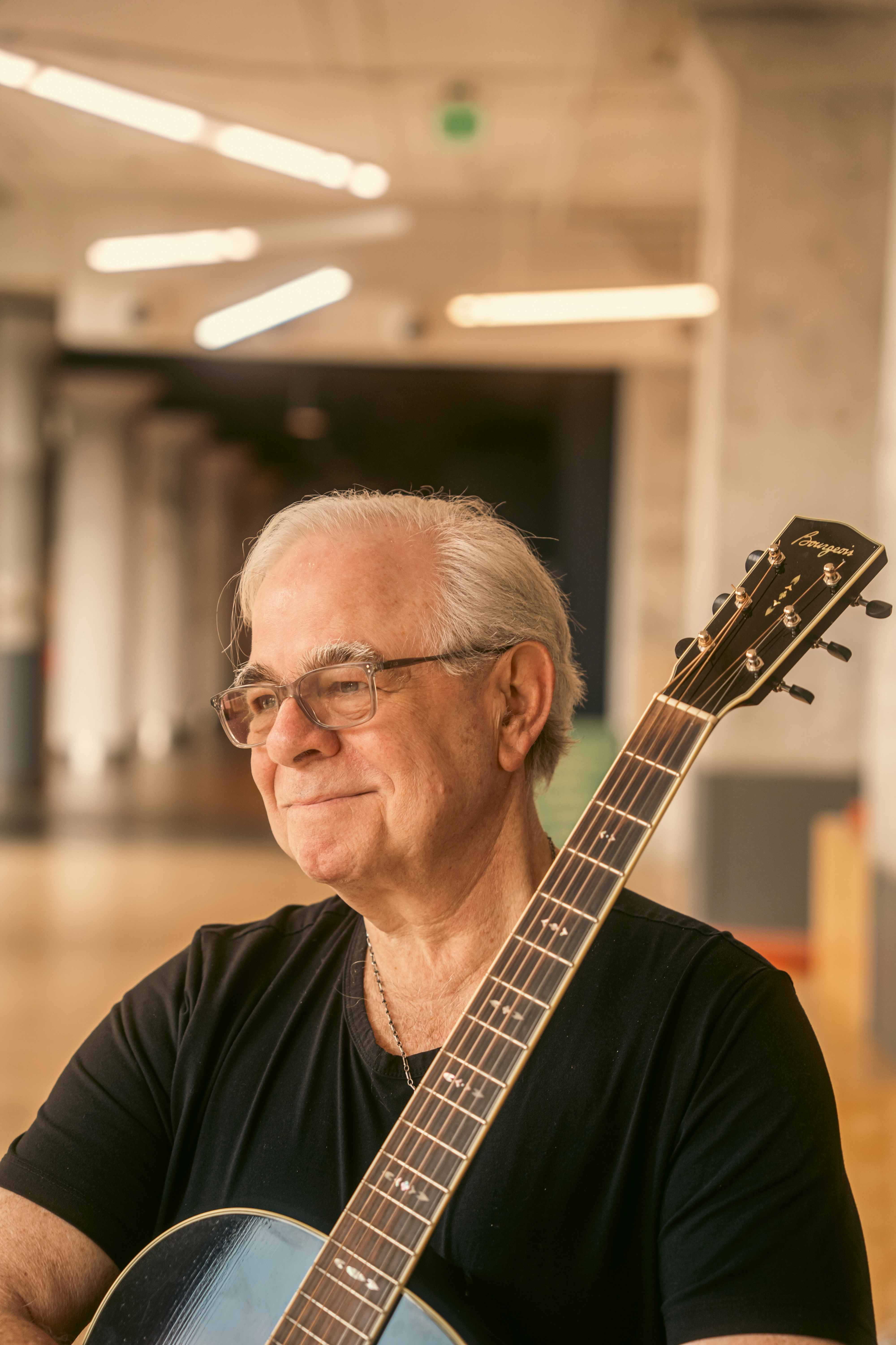 Dave Miller seated with his guitar and smiling in warm light